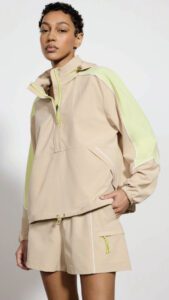 Woman in a beige hooded jacket and shorts with neon green details posing against a light background.