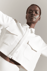 A young black woman in a stylish white jacket and pants, posing confidently against a neutral background.