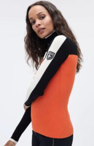 A woman in a stylish orange and black ribbed sweater posing sideways, looking at the camera.