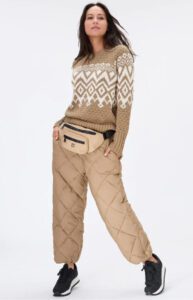 Woman wearing a patterned sweater and quilted pants, accessorized with a belt bag, standing in a casual pose against a plain background.